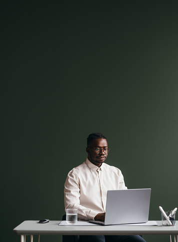 A mixed-race African-American entrepreneur typing on his laptop while sitting at the office desk. (grey background, copy space)