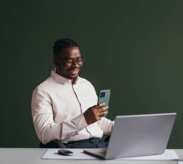istock A Happy Businessman With Glasses Texting On His Mobile Phone While Working On His Computer In The Office 1473801303