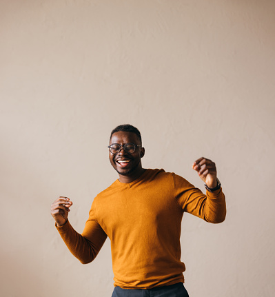 An excited mixed-race African-American entrepreneur laughing and dancing while standing against white background. (studio shot, copy space)