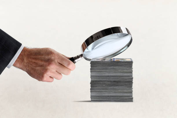 istock Man Holding Magnifying Glass Over Stack Of Money 1473805755