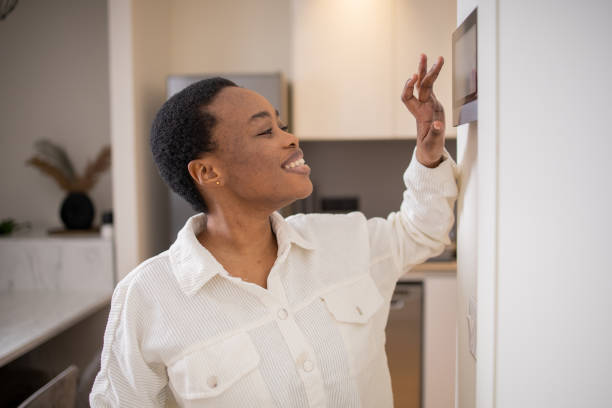 istock Young woman adjusts the temperature at home with a device on the wall 1473806400