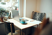 Laptop, documents and coffee shop with a table and chairs in an empty restaurant for freelance or remote work. Business, cafe and coffee with a pen and paper in a workspace at an internet cafe