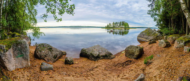 Stones on the shore and island with pine forest in beautiful fresh blue lake, Park Mon Repos, Vyborg, Russia.