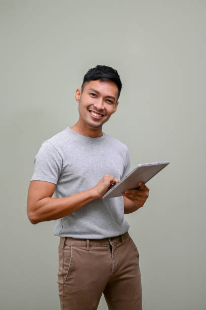istock Handsome Asian man holding a tablet and standing against an isolated green background. 1473813624