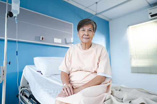 Senior woman in hospital gown with contented emotions sitting on hospital bed