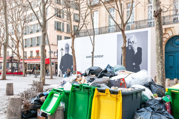 Grève des éboueurs : Full garbage bins during a waste collection strike in Paris, in the chic 6th arrondissement, in Saint Sulpice quarter, in front of a luxury store Yves Saint Laurent - France. March 15, 2023.