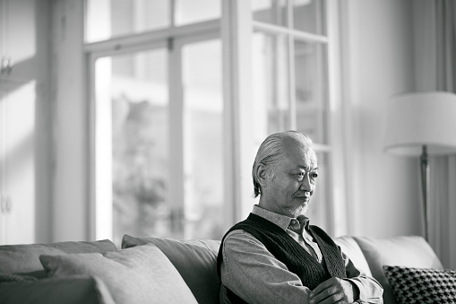 sad asian old man sitting alone on couch in living room at home, black and white