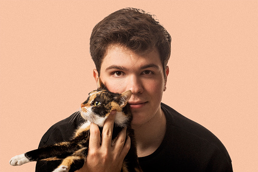 cat and young boy. Isolated pink background. Calico cat. Studio shoot. Cat and man hugging. Happy image.