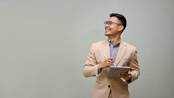 Smiling Asian businessman looking aside at the empty space, holding a tablet stock photo