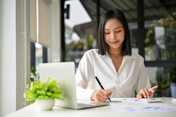 istock Professional Asian businesswoman writing something on financial reports, analyzing sales data 1473820979