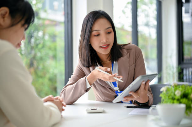 Focused Asian businesswoman using tablet, discussing work and working with her colleague stock photo
