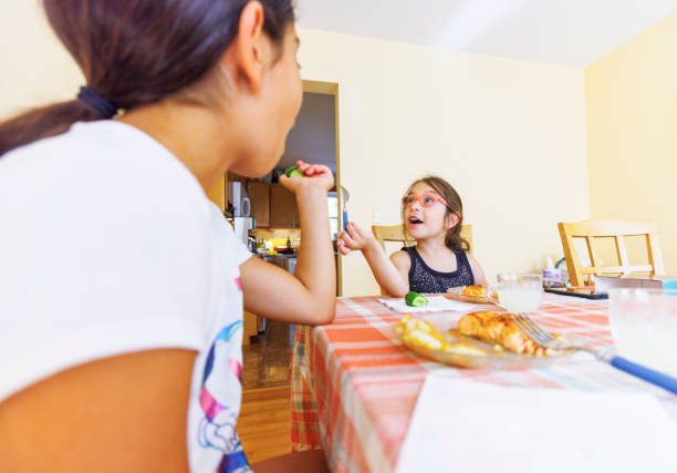 Two little sisters having dinner in the kitchen and talking.