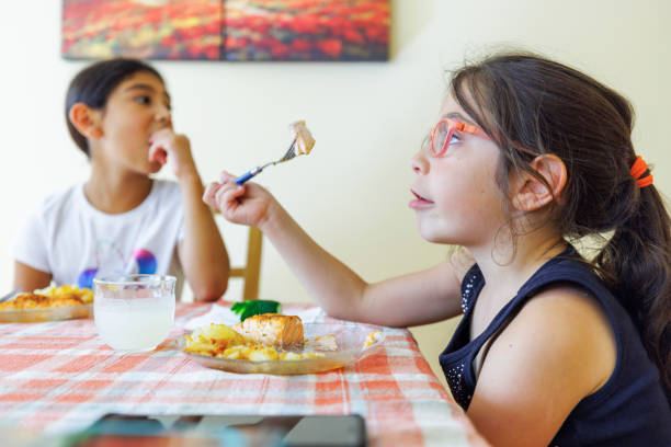 istock Funny, little girls indulging, while eating dinner at the kitchen table. Focus on the foreground, with defocused background. 1473829708