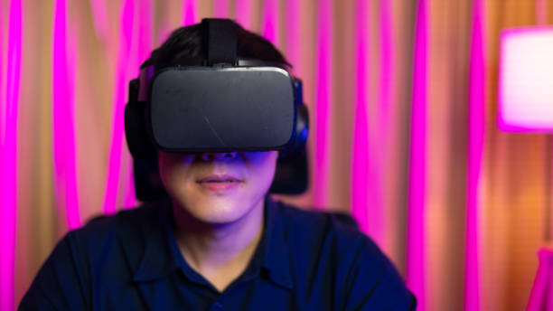 istock VR Headset. Asian man playing game on mobile phone with 3D simulation VR headset. Colorful neon light room. Esport online game. 1473830714