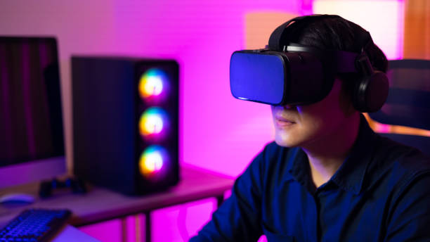 istock VR Headset. Asian man playing game on mobile phone with 3D simulation VR headset. Colorful neon light room. Esport online game. 1473830754