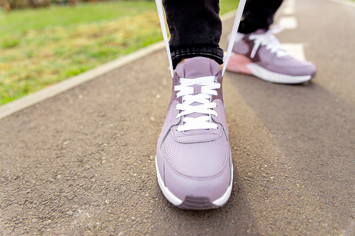 woman in sneakers stands on path and ties her shoelaces. Womens legs in pink sneakers close up