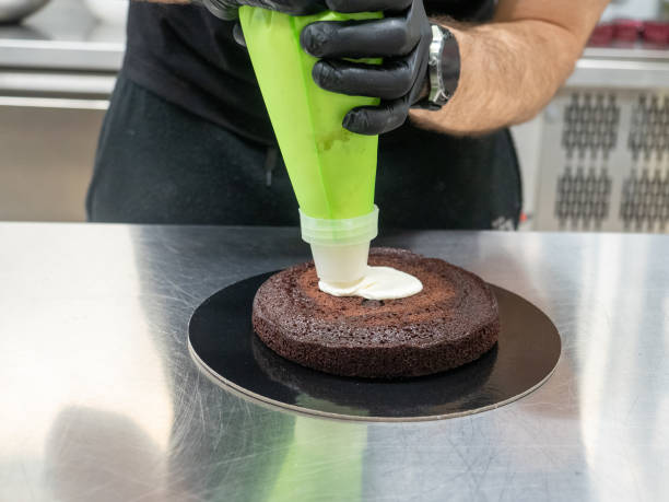 шеф-повар-пекарь готовит начиночный мешок с сливочным кремом для капания производства замороженного торта на кухне пекарни - cupcake chocolate icing candy стоковые фото и изображения