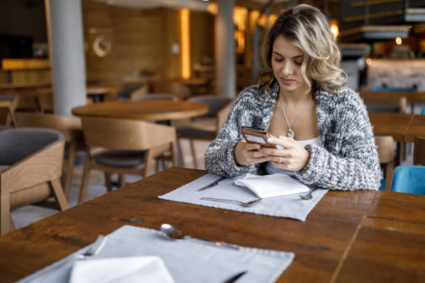 istock Beautiful young woman using phone at restaurant 1473840463