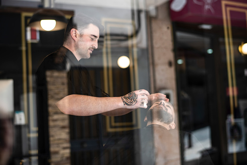 A barber cuts and shaves his client through the window