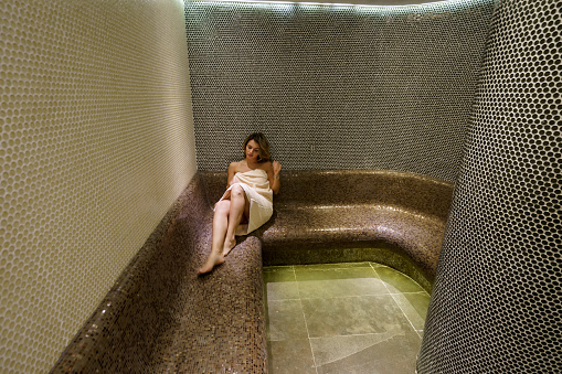 Full length shot of young woman sitting and relaxing in the steam room at the spa center