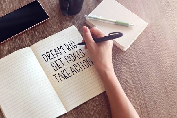 Dream big, set goals, take action. Business women writing text on notebook.