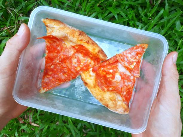 Hand holding Leftover Pizza in plastic container.