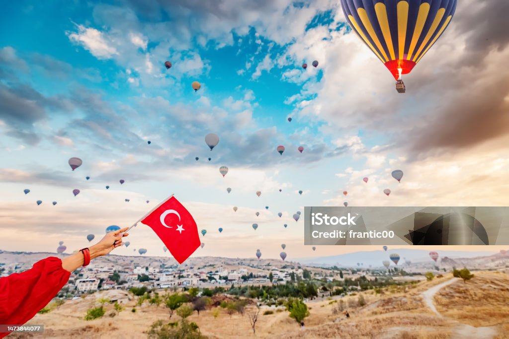 Experience the beauty and culture of Turkey through the eyes of a young woman as she watches the hot air balloons of Cappadocia soar and displays the Turkish flag. Adult Stock Photo