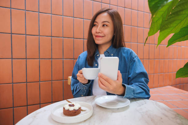 istock Portrait image of a young woman holding and using mobile phone while drinking coffee in cafe 1473845595