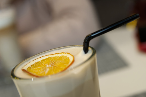 A slice of orange lies on the milk foam of a coffee drink in a glass cup