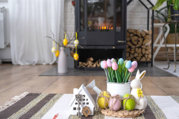 clé pour maison près de cheminée poêle avec feu et bois de chauffage. foyer confortable avec décor de pâques, œufs colorés dans un panier et lapin. construction, déménagement, hypothèque, location et achat immobilier, assurance - key house house key green photos et images de collection