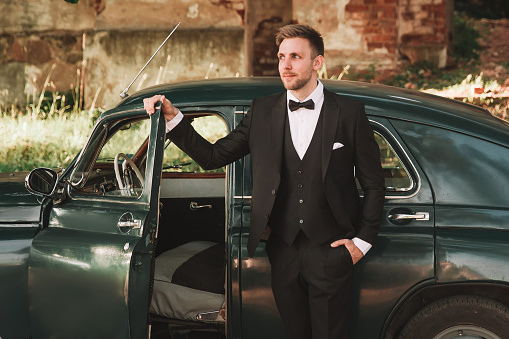 handsome groom, coming out of a vintage car . wedding in retro style