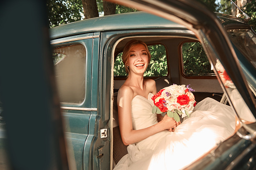 happy bride with bouquet sitting in car. wedding in retro style