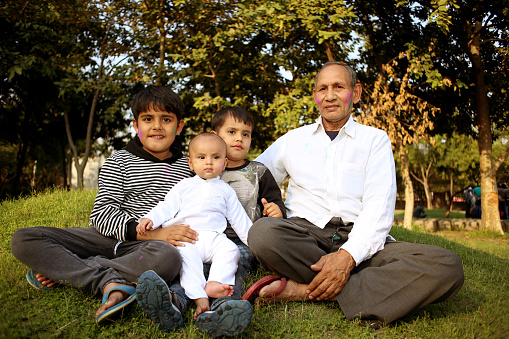 Children sitting with Grandfather in public park outdoors, Delhi, India.