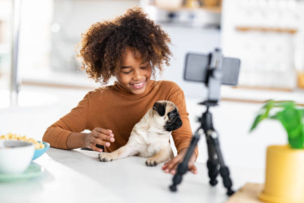 Happy black girl playing with her dog while vlogging over cell phone.