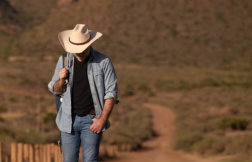 Adult man in cowboy hat walking on dirt road