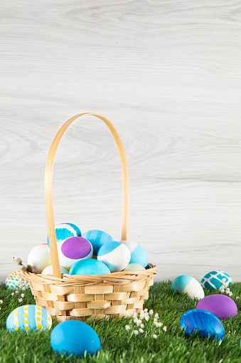 Easter eggs in a nest and small beautiful flowers behind a nest on empty rustic wooden table with defocused sunlight at background. Easter composition with copy space. Spring backdrop with bokeh for product display on top of the table.