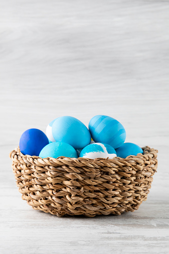 Pastel colored dyed Easter eggs in a basket on white rustic background.