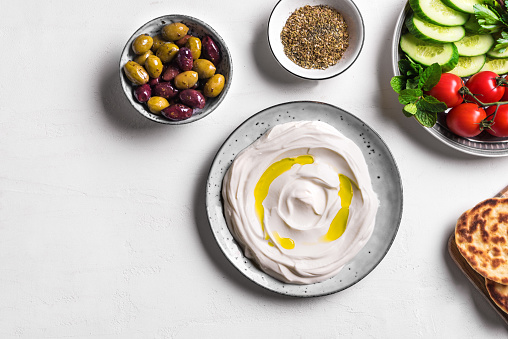Labneh yogurt cream cheese with olive oil, zaatar, olives, vegetables and pita bread on white background, copy space. Traditional arabian or middle eastern breakfast with labneh dip.
