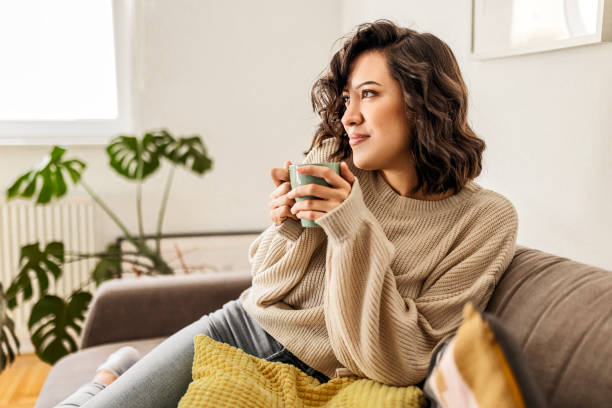 istock Young woman relaxing at home sitting on sofa drinking coffee 1473859801