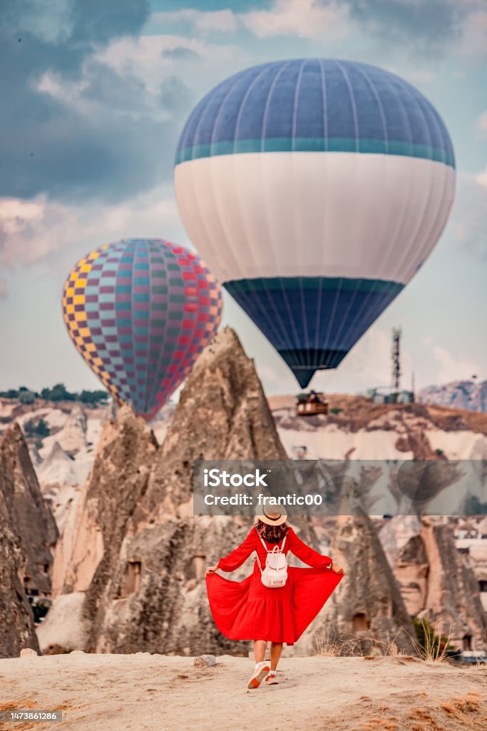 Mesmerised by the floating air balloons, the girl remained still as if in a trance, her dress a vibrant red against the orange sandstone of Cappadocia. 30-34 Years Stock Photo