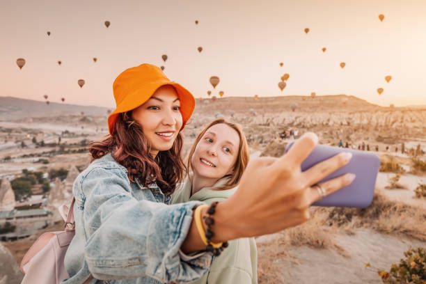 deux amies heureuses prenant des photos selfie sur smartphone en cappadoce, en turquie. concept de voyage et de médias sociaux - hot air balloon flying heat people photos et images de collection
