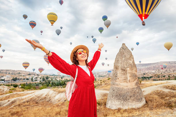 une fille en robe absorbée par la vue à couper le souffle des montgolfières en cappadoce, le paradis du voyageur. - hot air balloon flying heat people photos et images de collection