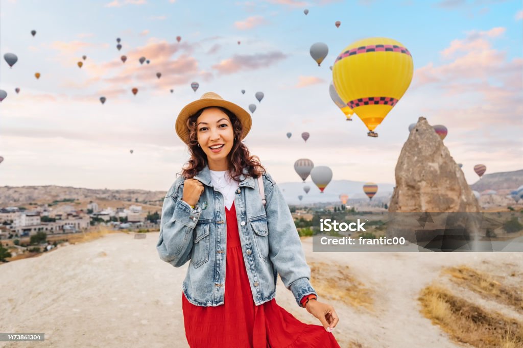 Girl traveler in her dress takes a breath of desert air, among the colorful balloons drifting through the Cappadocia sky. Basking in their beauty, she watches with a wide smile. 30-34 Years Stock Photo