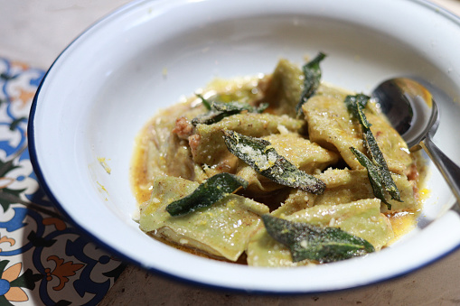 Close up a bowl of spinach agnolotti filled with mortadella & ricotta with lemon zest butter sauce in a restaurant