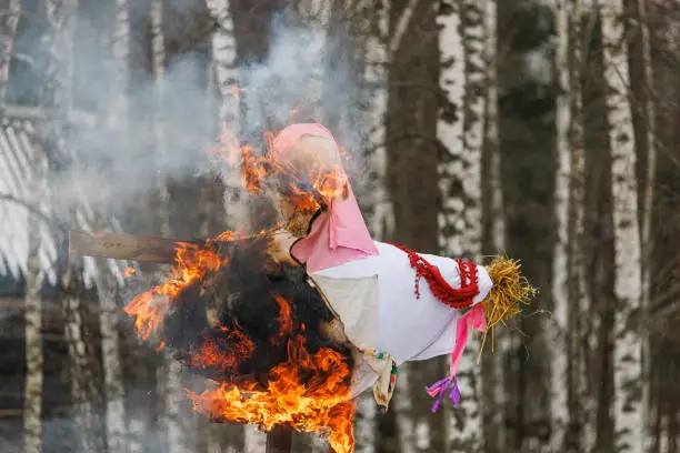 A burning large straw doll of a woman against the backdrop of trees. Little festivities. Holiday. Maslenitsa.