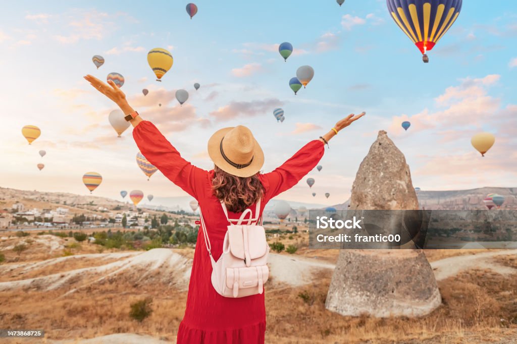 On a summer day in Cappadocia, Turkey, the girl in her pretty dress finds herself mesmerized by the elegant sight of air balloons in the sky. Rock Hoodoo Stock Photo