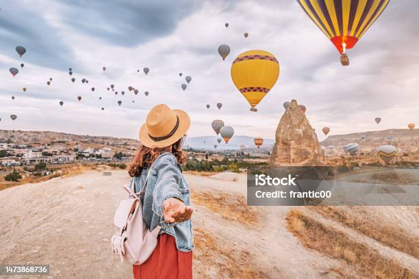 Join The Adventure In Cappadocia Turkey As A Young Woman Strikes A Confident Follow Me Pose With Hot Air Balloons Soaring In The Background Stock Photo - Download Image Now