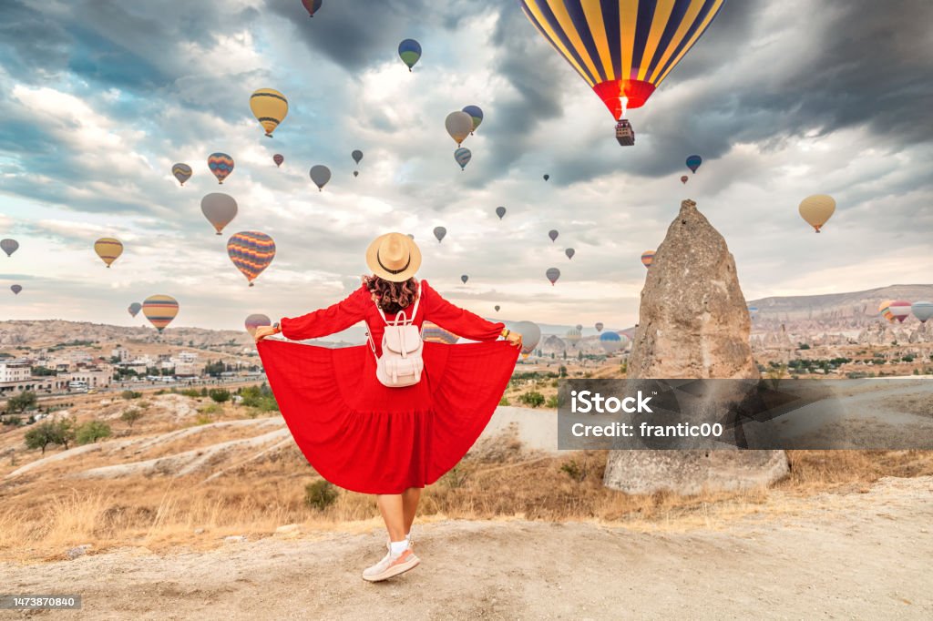 In the beautiful landscape of Cappadocia, the girl in her flirty dress finds joy in the sight of the air balloons, her dreams of travel conjured in the sky 30-34 Years Stock Photo