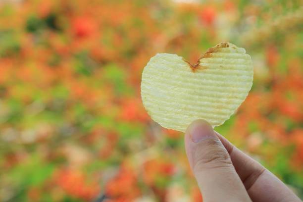 patatina a forma di cuore in mano di donna con foglie colorate in sfondo autunnale. - potato chip foto e immagini stock