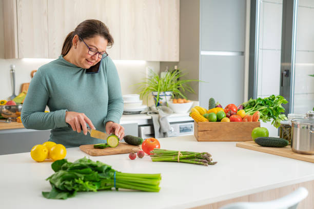 istock Woman holding mobile phone between ear and shoulder talking while chopping vegetables 1473874035